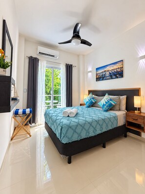 A modern hotel room with a large bed, a ceiling fan, a painting, and a view of greenery outside. - Luxury family villa with a private pool, spacious rooms, and top-notch amenities (Puerto Morelos)