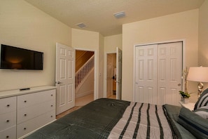 A bedroom with a bed, dresser, TV, and a staircase leading to another room. - 3BR Townhouse Near Disney Private Pool (Clermont)