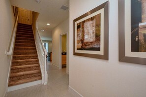 Un passadís amb una escala amb moqueta, un quadre a la paret i una cuina a la distància.