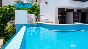 Ein Schwimmbecken mit gefliesten Rändern, einer Metallleiter und einem blauen Sonnenschirm.