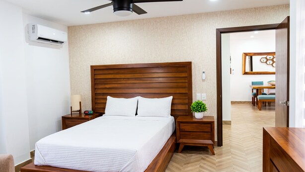 Ein Hotelzimmer mit einem hölzernen Bett, einem Nachttisch, einer wandmontierten Klimaanlage, einem Deckenventilator und Blick auf den Essbereich.