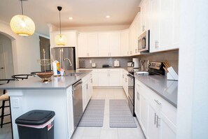 A modern kitchen with white cabinets, stainless steel appliances, and a central island. - 6BR Home w/ Pool, Theater & Game Room (Kissimmee)