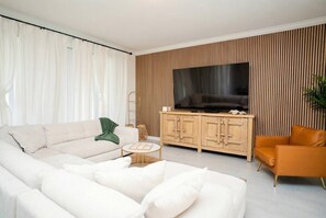 A modern living room with a sofa, a coffee table, a TV, and a cabinet. - 6BR Home w/ Pool, Theater & Game Room (Kissimmee)