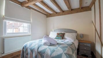 A bedroom with a bed, a nightstand, a window, and exposed wooden beams.