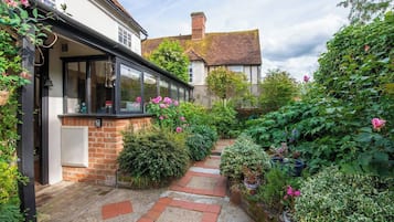 A garden pathway leading to a house with a brick wall and a window overlooking the garden.