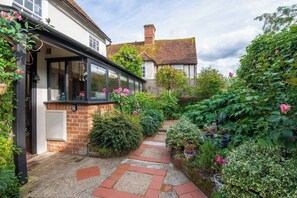 A garden pathway leading to a house with a brick wall and a window overlooking the garden.