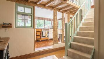A spacious room with a wooden staircase, a kitchen area with wooden cabinets, and a view of the outdoors.