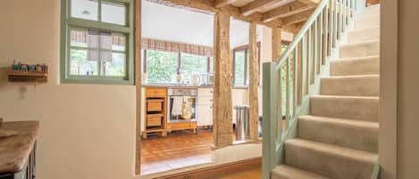 A spacious room with a wooden staircase, a kitchen area with wooden cabinets, and a view of the outdoors.