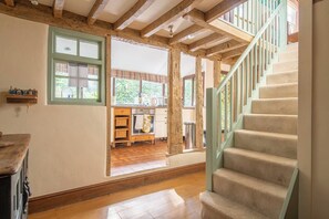 A spacious room with a wooden staircase, a kitchen area with wooden cabinets, and a view of the outdoors.