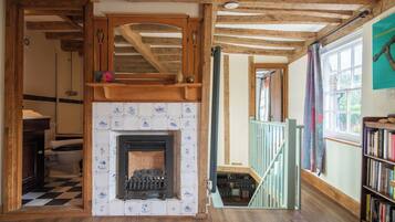 A room with a fireplace, wooden beams, a staircase, and a bookshelf.