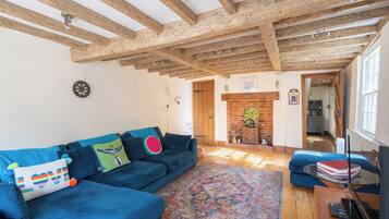 A room with a blue sofa, a patterned rug, wooden beams on the ceiling, a fireplace, and a television on a wooden table.