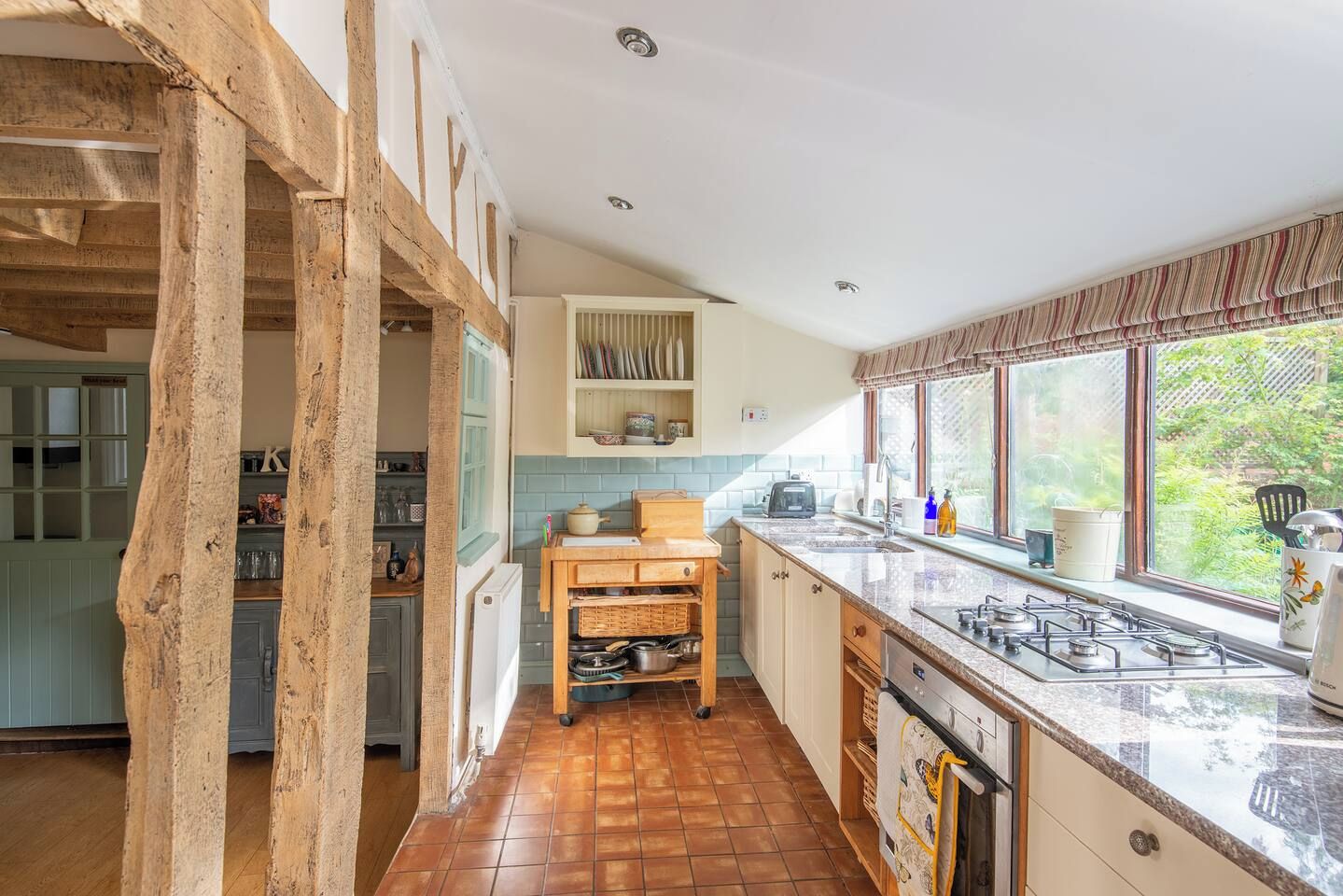 A kitchen with a gas stove, wooden cabinets, and a window with a view of greenery.
