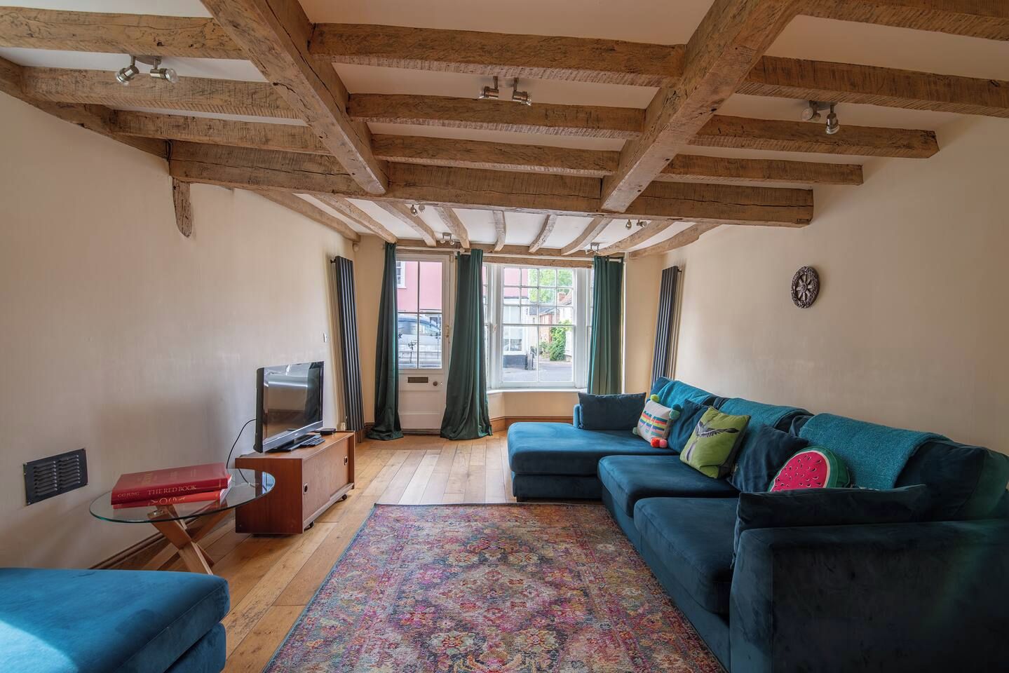 A living room with exposed wooden beams, a sofa set, a television, and a patterned rug.