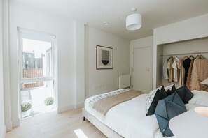 Un dormitorio con cama, lámpara colgante, cuadro enmarcado, radiador y perchero.