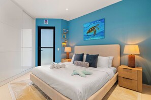 Un dormitorio con una cama grande, dos mesitas de noche con lámparas, una pared con cuadros enmarcados y una puerta.