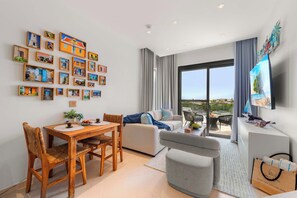 A modern living room with a dining area, a sofa, a TV, and a balcony with a view. - Top Floor Beach Condo|Near Eagle Beach|Pool&Jacuzzi (Pos Abou)