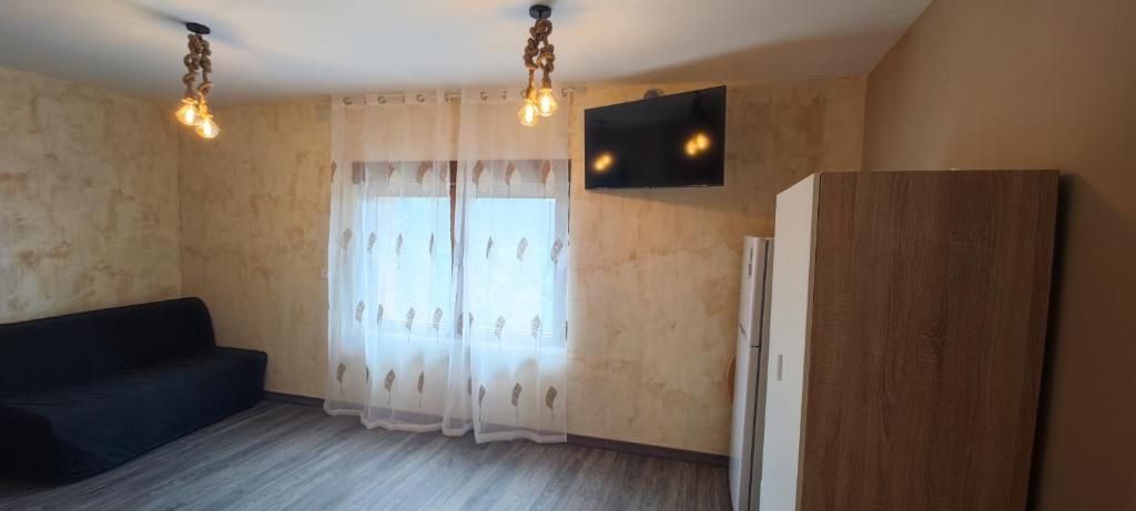 Ein Zimmer mit einer Couch, einem an der Wand befestigten Fernseher, einem Kühlschrank und einem Fenster mit Vorhängen.