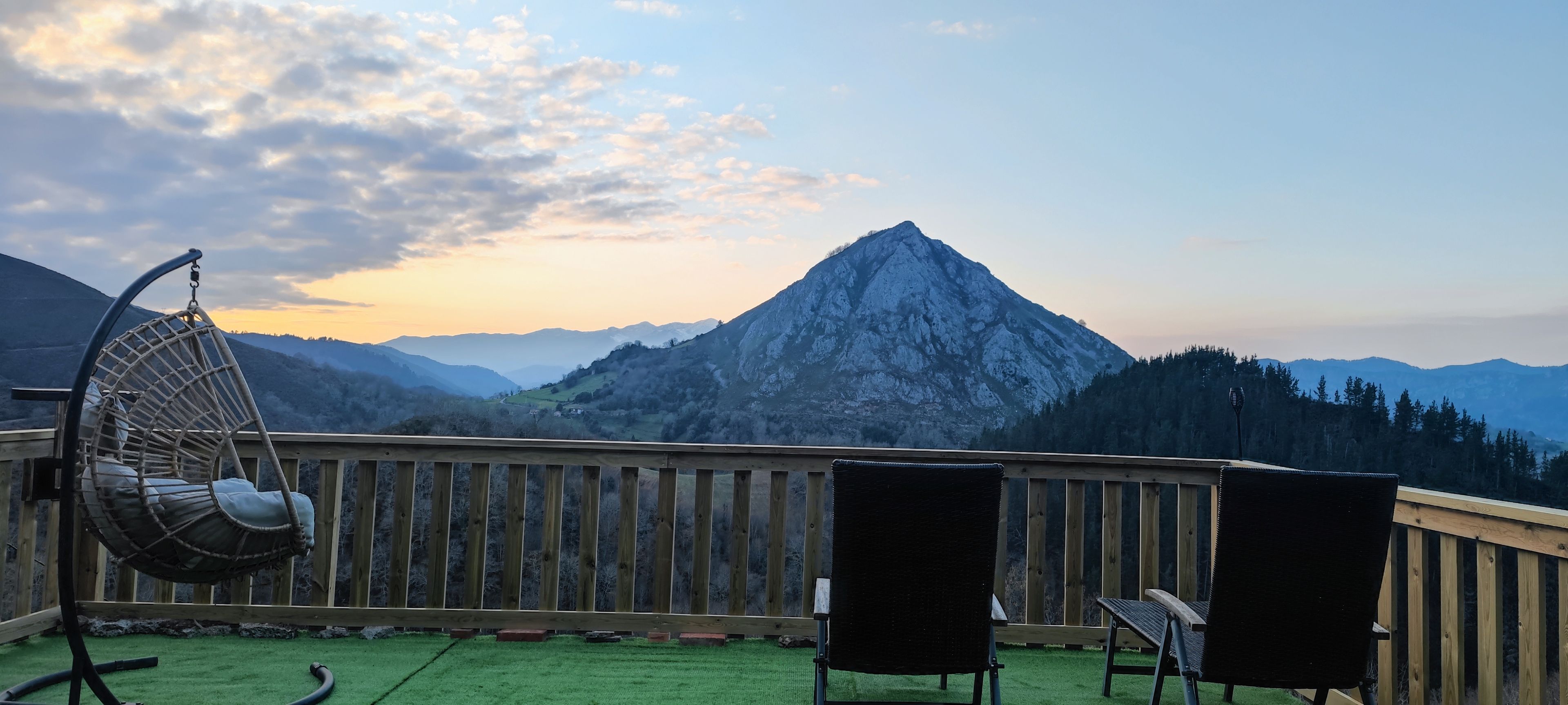 A balcony with a view of a mountain, a hanging chair, and two chairs.