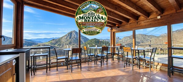 A restaurant with outdoor seating, wooden beams, and a view of mountains.