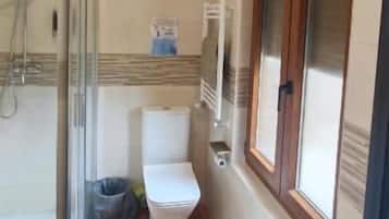 A bathroom with a toilet, shower, and a window.