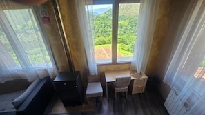 Habitación con vistas a un paisaje verde a través de amplios ventanales, una mesita con una silla y un armario negro.