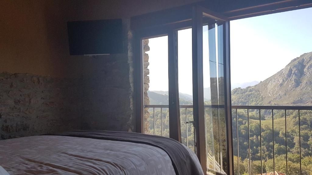 Een slaapkamer met een bed, een aan de muur bevestigde televisie en een groot raam met uitzicht op een bergachtig landschap.