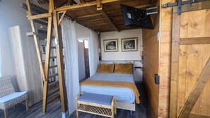A bedroom with a bed, a wooden ladder, a bench, and a door. - Granja Paraiso. Oasis Rural & Bienestar (Cangas de Onis)