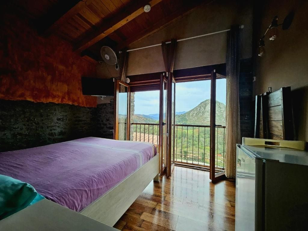 A bedroom with a bed, a wooden floor, a balcony with a view, and a refrigerator.
