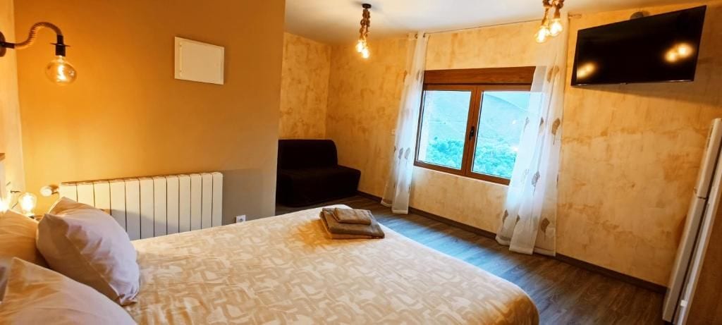 Un dormitorio con cama, una silla, un radiador, una ventana con cortinas y un televisor en la pared.