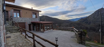 Un edificio con fachada de piedra, una escalera de madera y vistas a montañas.