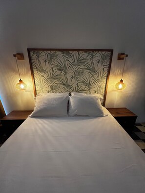 Ein Bett mit einem Kopfteil mit Blättermuster, flankiert von zwei Nachttischen mit Wandleuchten.