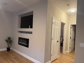 A hallway with a flat-screen TV mounted on the wall, a potted plant, and a door leading to another room.