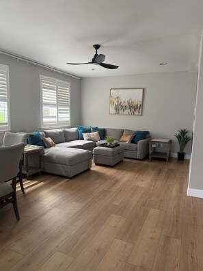 A modern living room with a sectional sofa, a small table, and a ceiling fan.