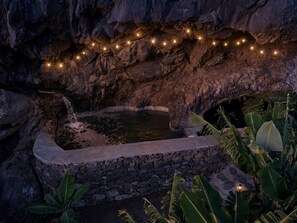 A natural rock formation with a water feature and string lights.