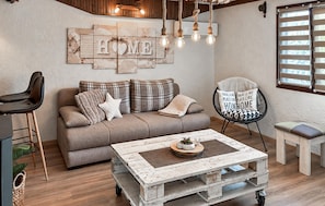 A cozy living room with a sofa, a coffee table, and a chair. There is a wall decoration with the word 'HOME' and a sign that says 'THERE IS NO PLACE LIKE HOMESHOME.'