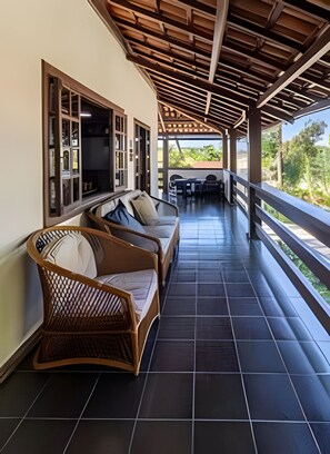 A covered outdoor seating area with wicker furniture and a view of the landscape. - Casa 1 Porto Seguro 6 Quartos e Piscina (Porto Seguro)