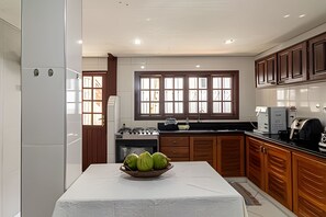 A modern kitchen with a central island, wooden cabinets, and a window with multiple panes. - Casa 1 Porto Seguro 6 Quartos e Piscina (Porto Seguro)