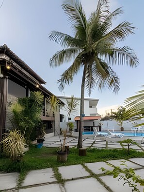 A residential property with a swimming pool, a palm tree, and a modern house with a thatched roof. - Casa 1 Porto Seguro 6 Quartos e Piscina (Porto Seguro)