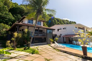 A two-story building with a swimming pool, surrounded by lush greenery and a clear sky. - Casa 1 Porto Seguro 6 Quartos e Piscina (Porto Seguro)