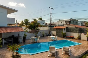 A swimming pool with lounge chairs and a table, surrounded by a wooden deck and potted plants. - Casa 1 Porto Seguro 6 Quartos e Piscina (Porto Seguro)