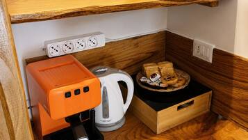 Eine Küchenzeile mit Kaffeemaschine, Wasserkocher und Brötchenkorb auf einer Holzausziehtafel.