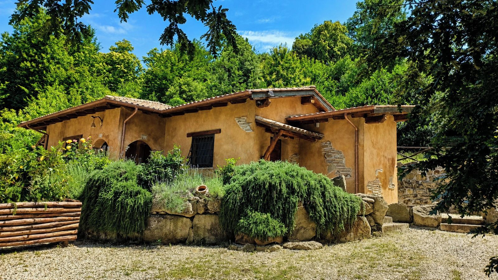 Un bâtiment de style rustique, doté d’un toit en tuiles, de murs en pierre et d’un jardin agrémenté de diverses plantes et d’une clôture en bois.