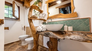 Un bagno con uno scaffale a forma di albero in legno che contiene asciugamani, un lavandino bianco e uno schienale piastrellato verde.