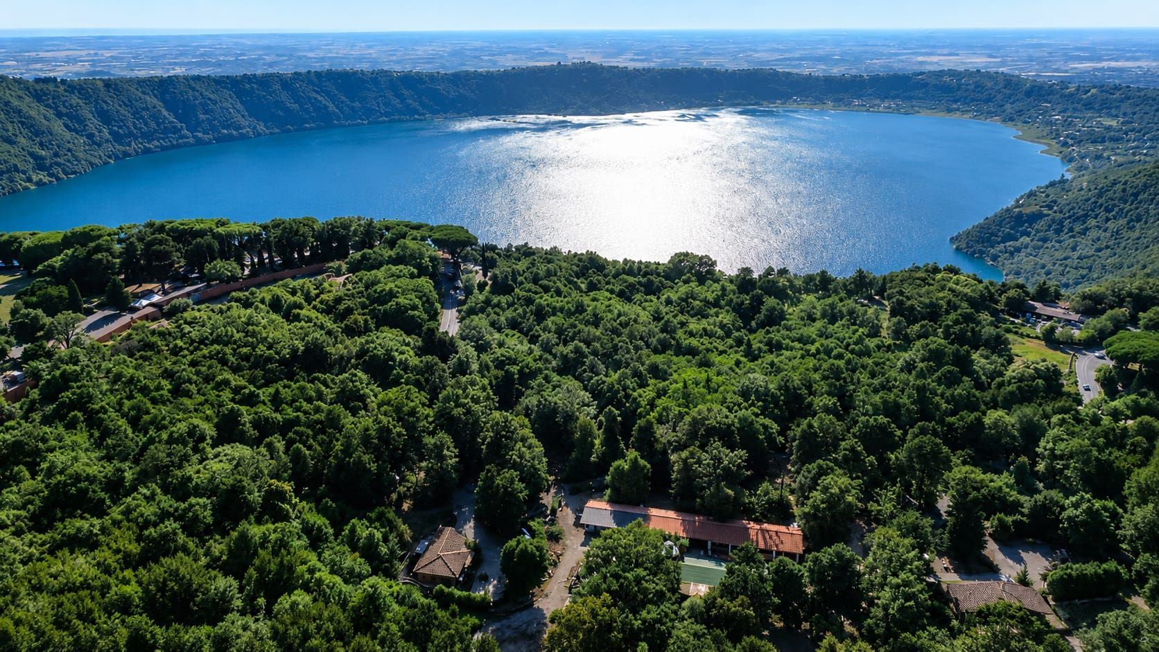 Une vue aérienne d’une zone côtière, avec une étendue d’eau importante, une végétation luxuriante et quelques bâtiments aux toits rouges.