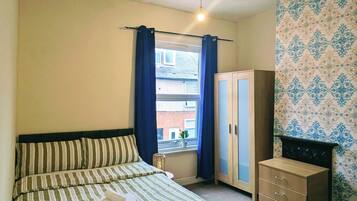 A bedroom with a bed, a wardrobe, a window with curtains, and a patterned wall.