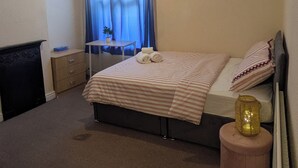 Quarto com cama, mesa de cabeceira e um banquinho.