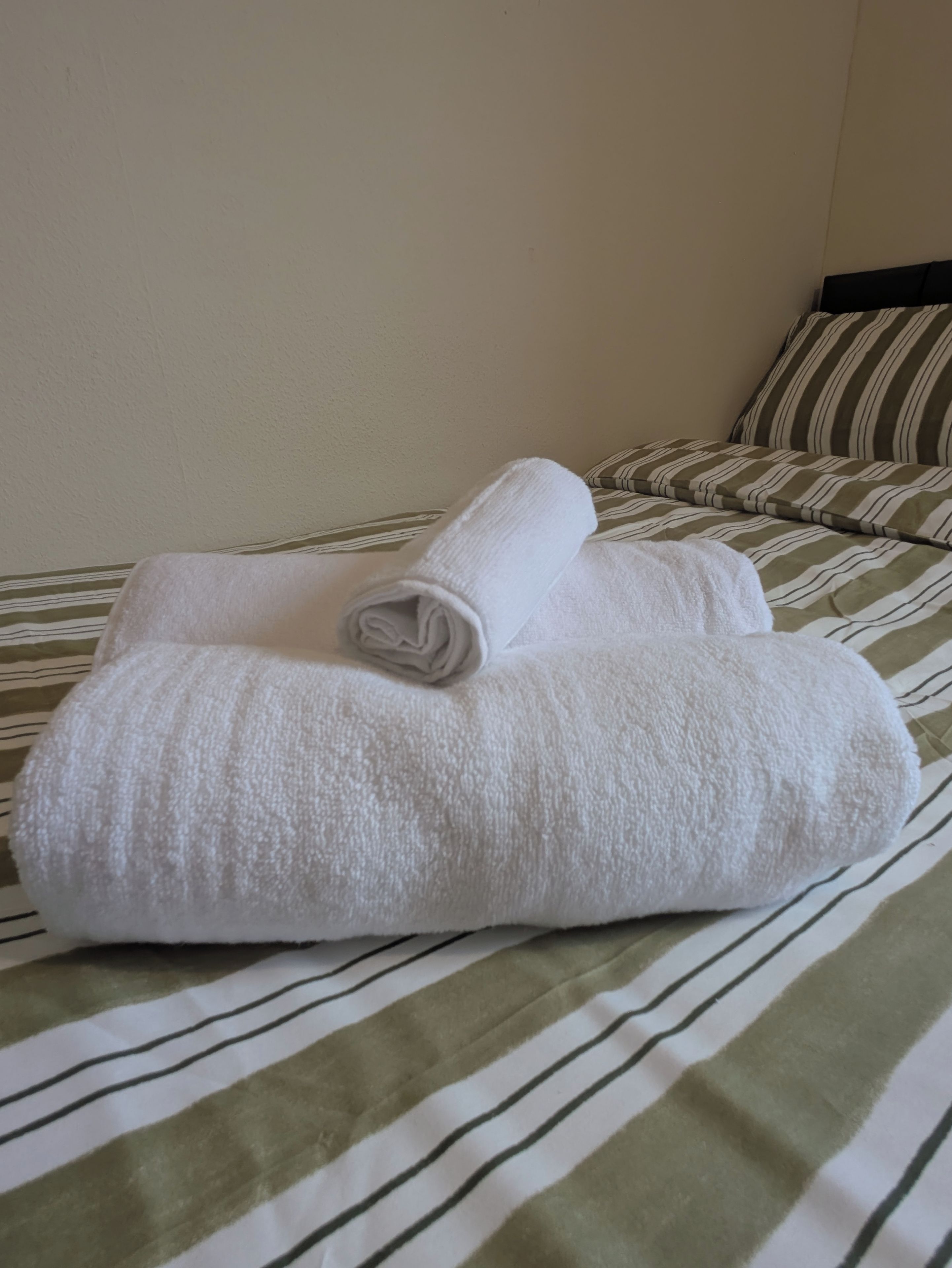 Una cama con una colcha a rayas y dos toallas blancas enrolladas.
