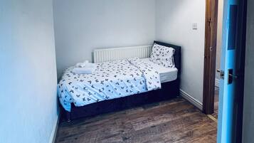A small, single-bed room with a wooden floor, a white radiator, and a hanging lamp.