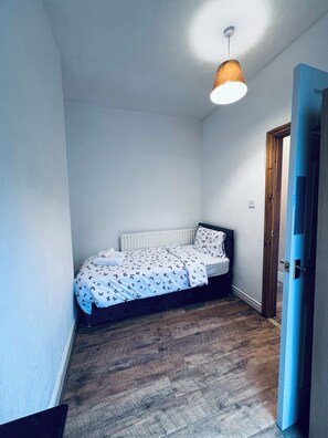 A small, single-bed room with a wooden floor, a white radiator, and a hanging lamp. - 6 minutes drive from Coventry city centre!
For families,contractors & travelers (Coventry)