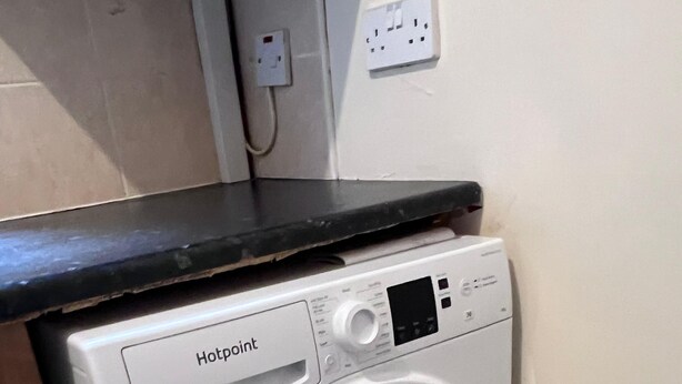 Máquina de lavar roupa Hotpoint de abertura frontal, com painel de comandos, colocada num canto de um espaço com chão em mosaico.